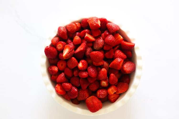 White pie dish with chopped strawberries on white background