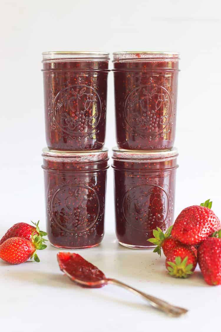 4 Jars of strawberry jam with strawberries in background and spoon