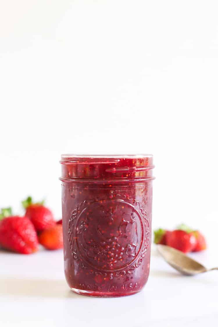 Jar of strawberry jam with strawberries in background and spoon