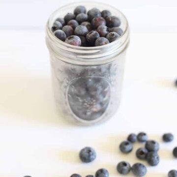 Ball mason jar of frozen blueberries on white background