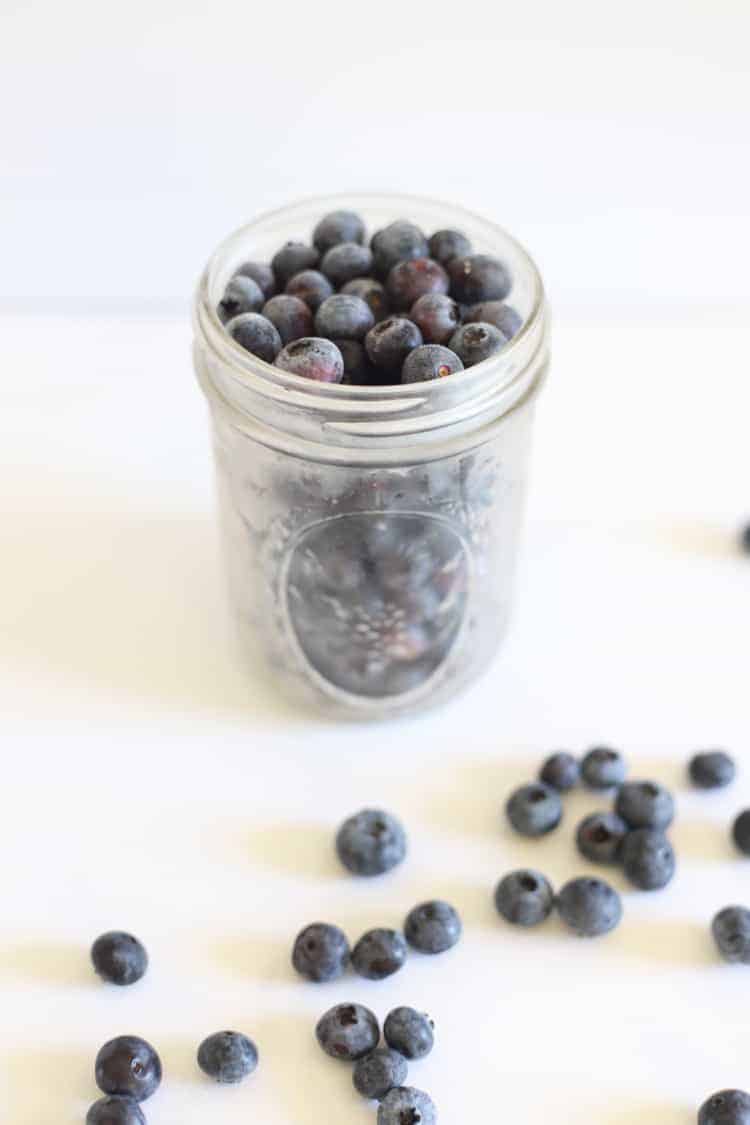 Ball mason jar of frozen blueberries on white background