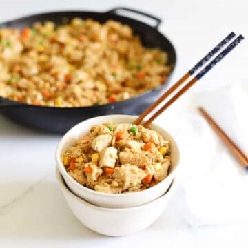 Chicken fried rice in a bowl with chopsticks and pan of fried rice in the background