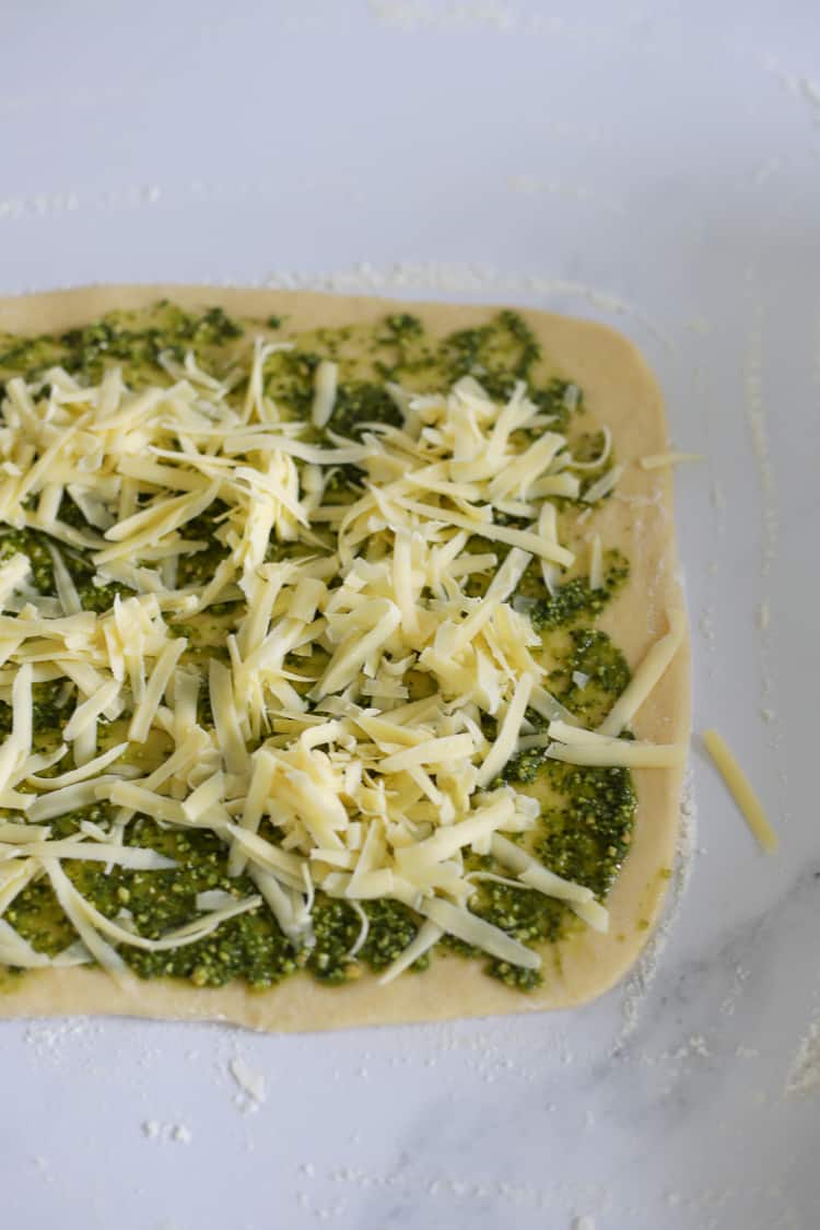 Dough spread with pesto and topped with grated cheese