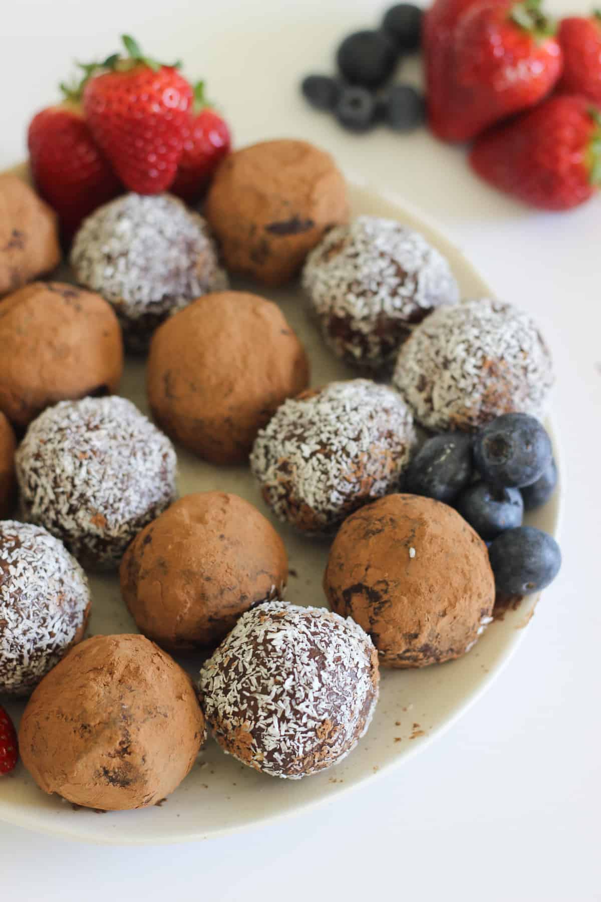 Chocolate truffles on white plate. Strawberries in background
