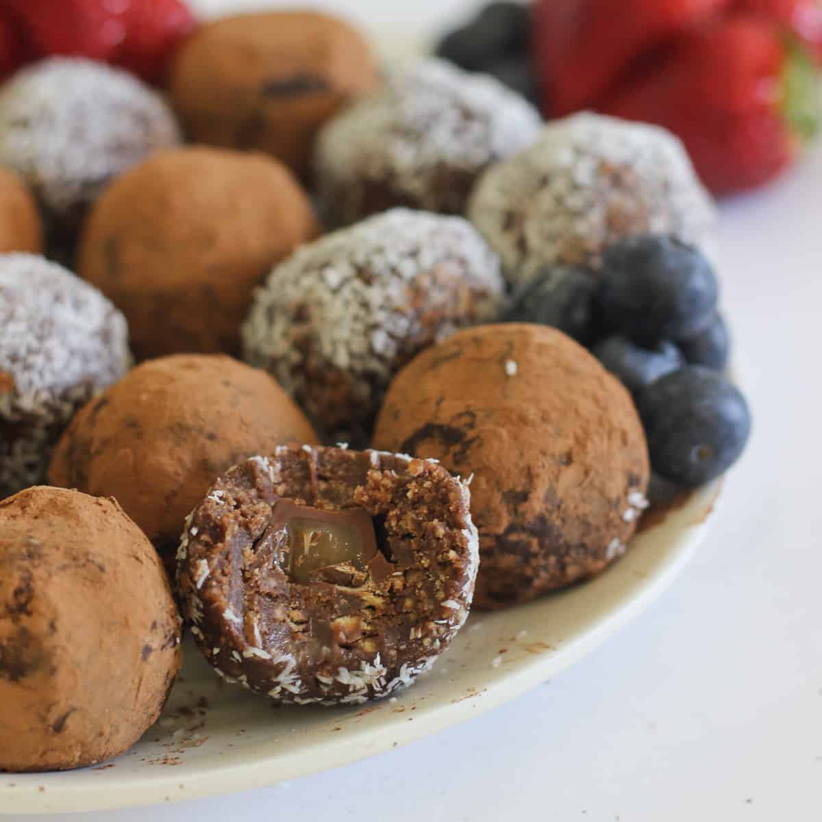 Chocolate truffles on white plate, one with bite taken out. Strawberries in background.