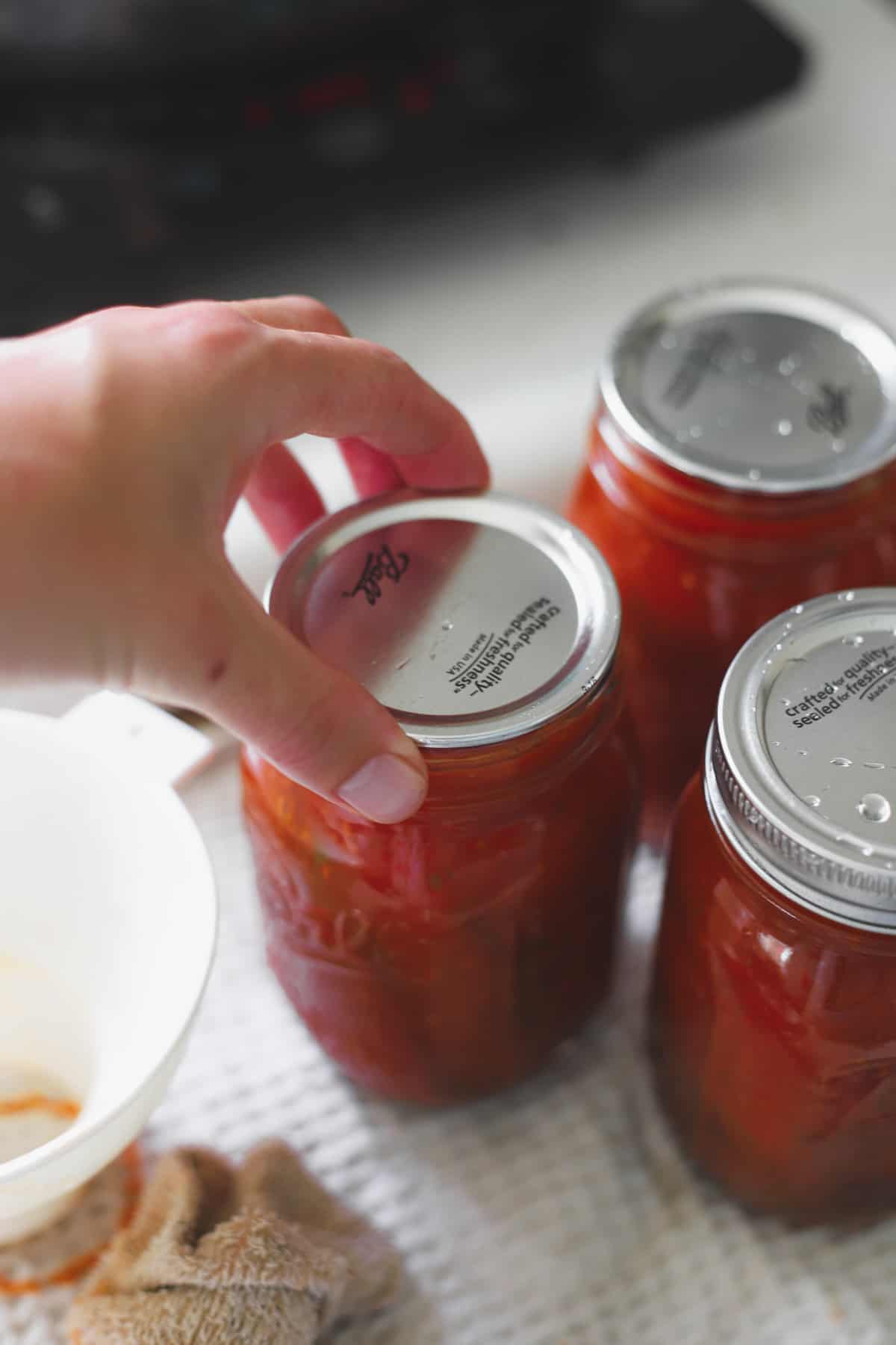 Hand placing canning lid on jar of tomatoes