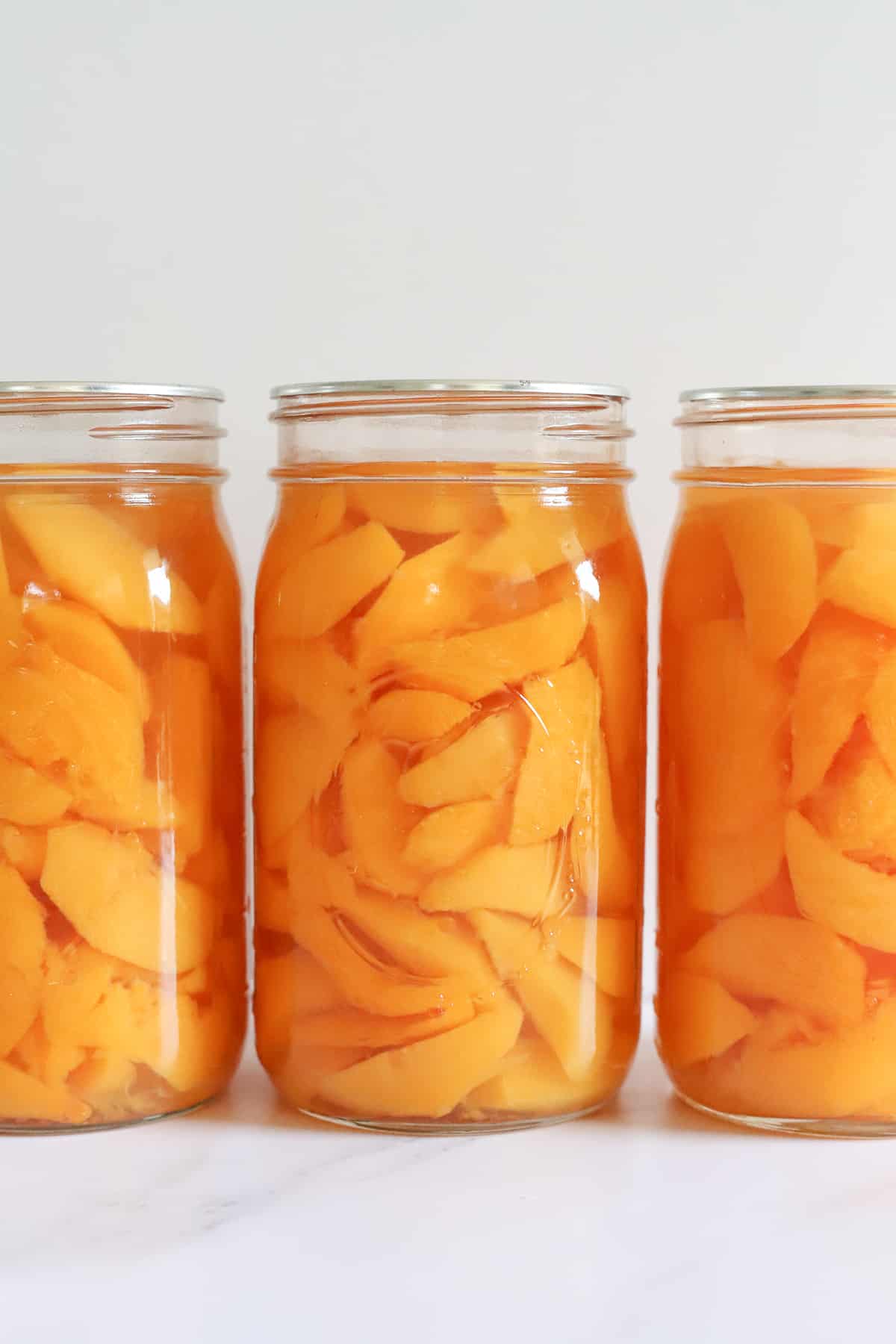 3 quart jars of peaches on a white background