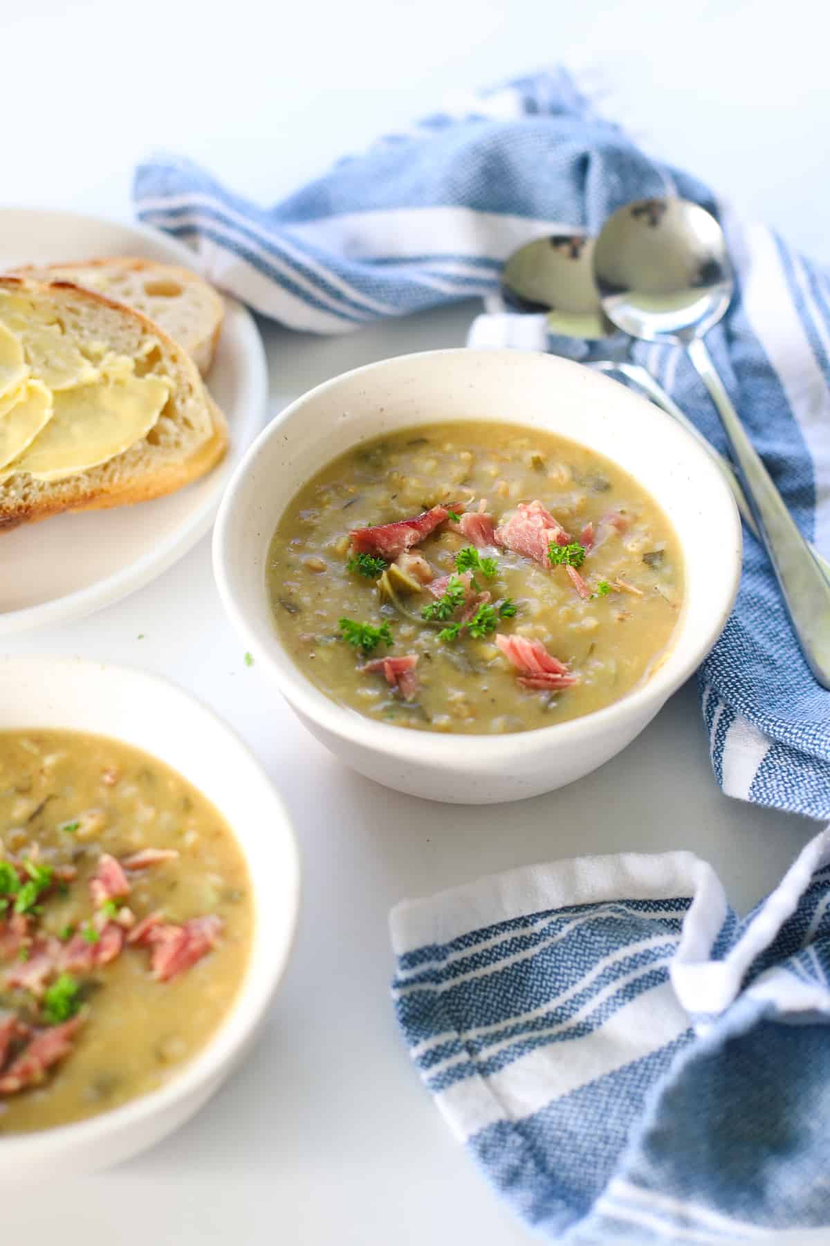 Two bowls of bacon bone and vegetable soup on table with slice of buttered bread