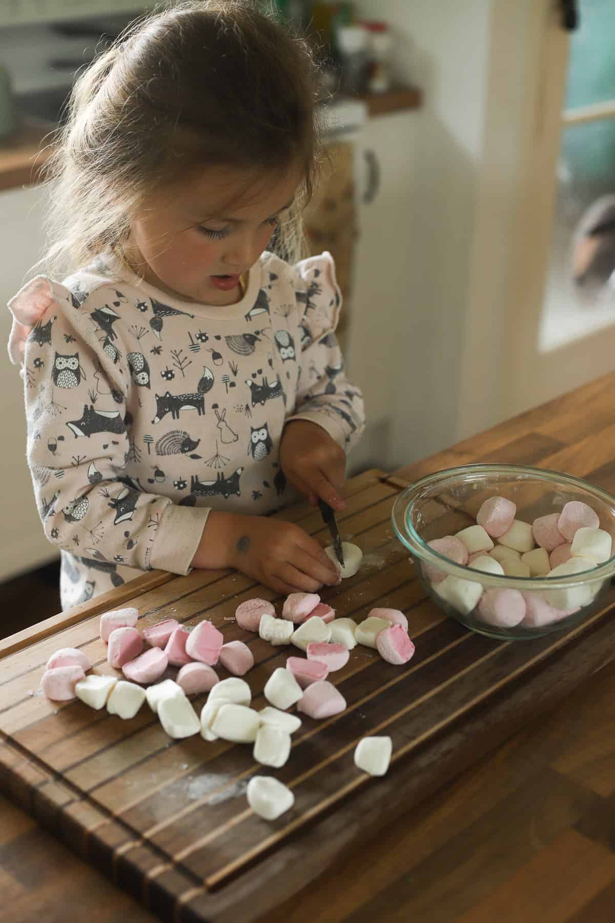 Colorful marshmallows being cut by a young girl in a cozy kitchen setting.